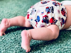 Auf dem Bild ist ein Baby auf dem Bauch liegend zu sehen, es trägt eine Stoffwindel mit Eulenprint. Das Gesicht des Babies ist nicht auf dem Bild.